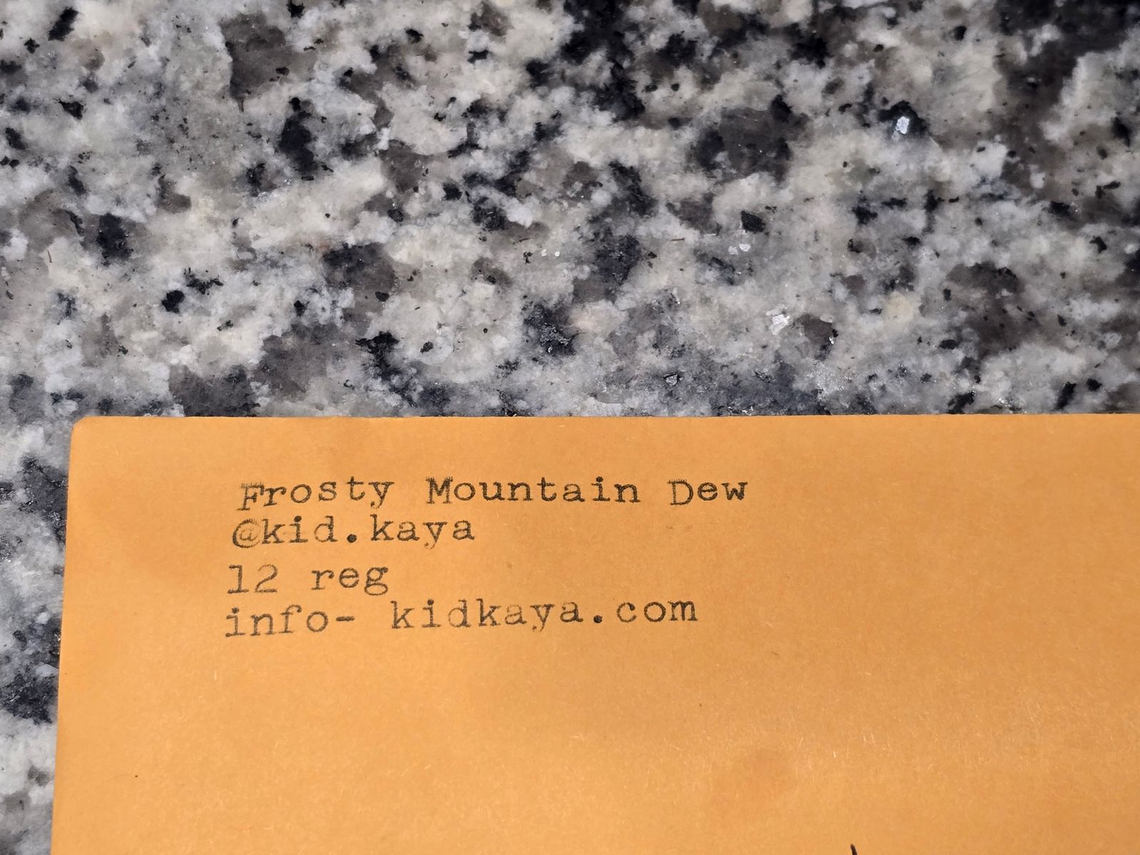 Orange business card on granite surface showing contact details for Frosty Mountain Dew including social media handle, registration number and website
