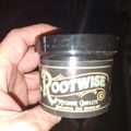 A hand holding a clear glass jar with a black label that reads "Rootwise Mycorise Complete" botanical soil inoculant