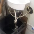 A white toilet with plumbing connections and a black container underneath in a bathroom setting
