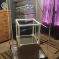 A white PVC pipe frame structure with pulleys and cables set up in a bedroom, positioned on a patterned rug near a bed and wooden dresser.