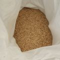 A white plastic bag containing brown rice grains or similar small grain seeds