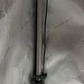 A close-up view of a metal pole or stand with green securing bands or clamps attached to it, positioned against a textured mesh or fabric background