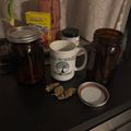 Kitchen counter with mason jars, a white mug with tree logo, and various items including what appears to be dried plant material