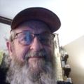Man with long gray beard wearing glasses and a dark beret hat taking a selfie indoors