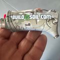 A person holding a metallic toy or model gun with "BUILDSOIL.COM" text and decorative engravings on its surface