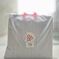A gray fabric shopping bag with red handles and a circular logo label that reads "COWOCO" sits on a white surface