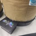 A beige suede boot resting on a dark electronic device with colorful logo text on a white surface