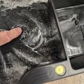 A finger pointing at water flowing down a sink drain with water droplets visible on the surface