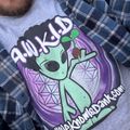 A person wearing a gray t-shirt with a cartoon alien character design and text, along with a blue plaid flannel shirt over it
