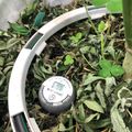 A digital soil moisture meter device placed in a garden bed among green seedlings and plant debris