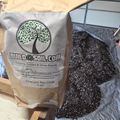 A bag of BuildASoil.com Charged Bio Char garden soil amendment with dark granular biochar material spilled on plastic sheeting beside it