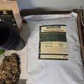 A bag of BuildAFlower Top Dress soil blend sits on a wooden surface next to gardening supplies including plant pots and organic material