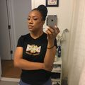 A woman taking a mirror selfie in a bathroom wearing a black t-shirt and blue shorts